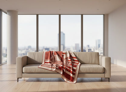 Beige sofa with a red and white patterned blanket in a room with large windows.