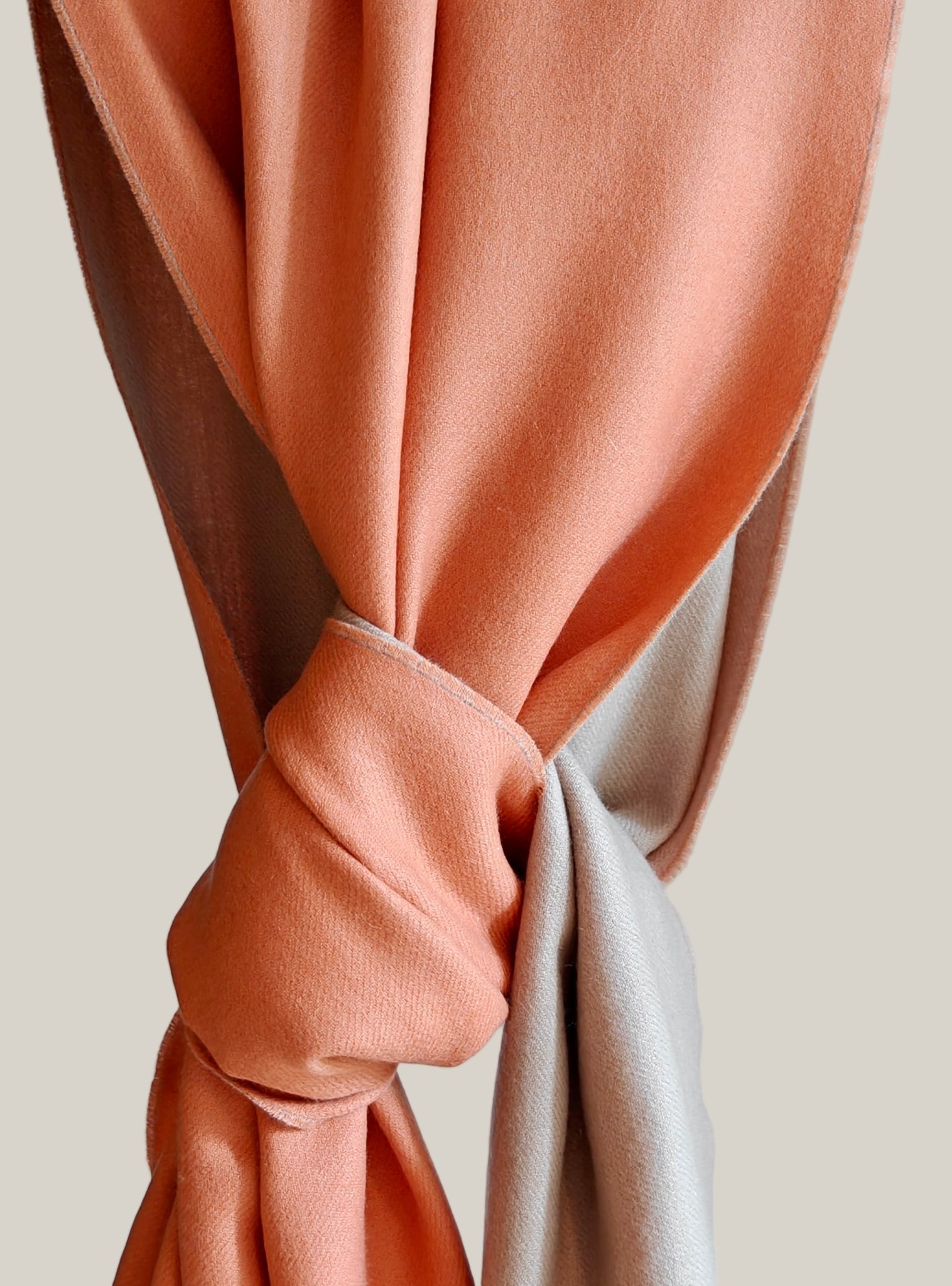 Close-up of a peach-colored curtain tied back against a light blue wall.