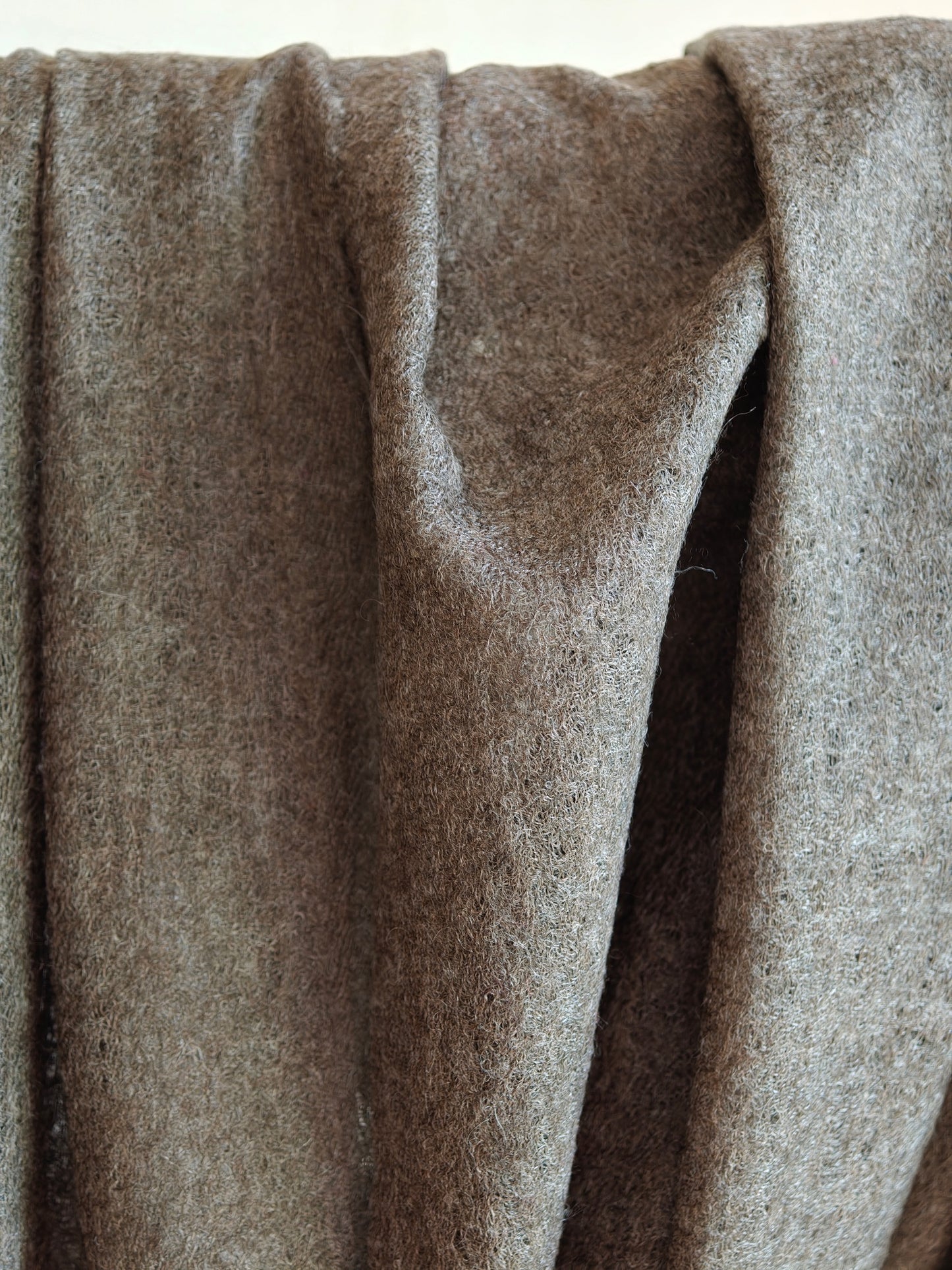Detailed view of a lightweight brown cashmere shawl showing its semi sheer weave, airy texture, and natural wool fibers. Light filtering through the fabric emphasizes its breathability, softness, and handcrafted quality.