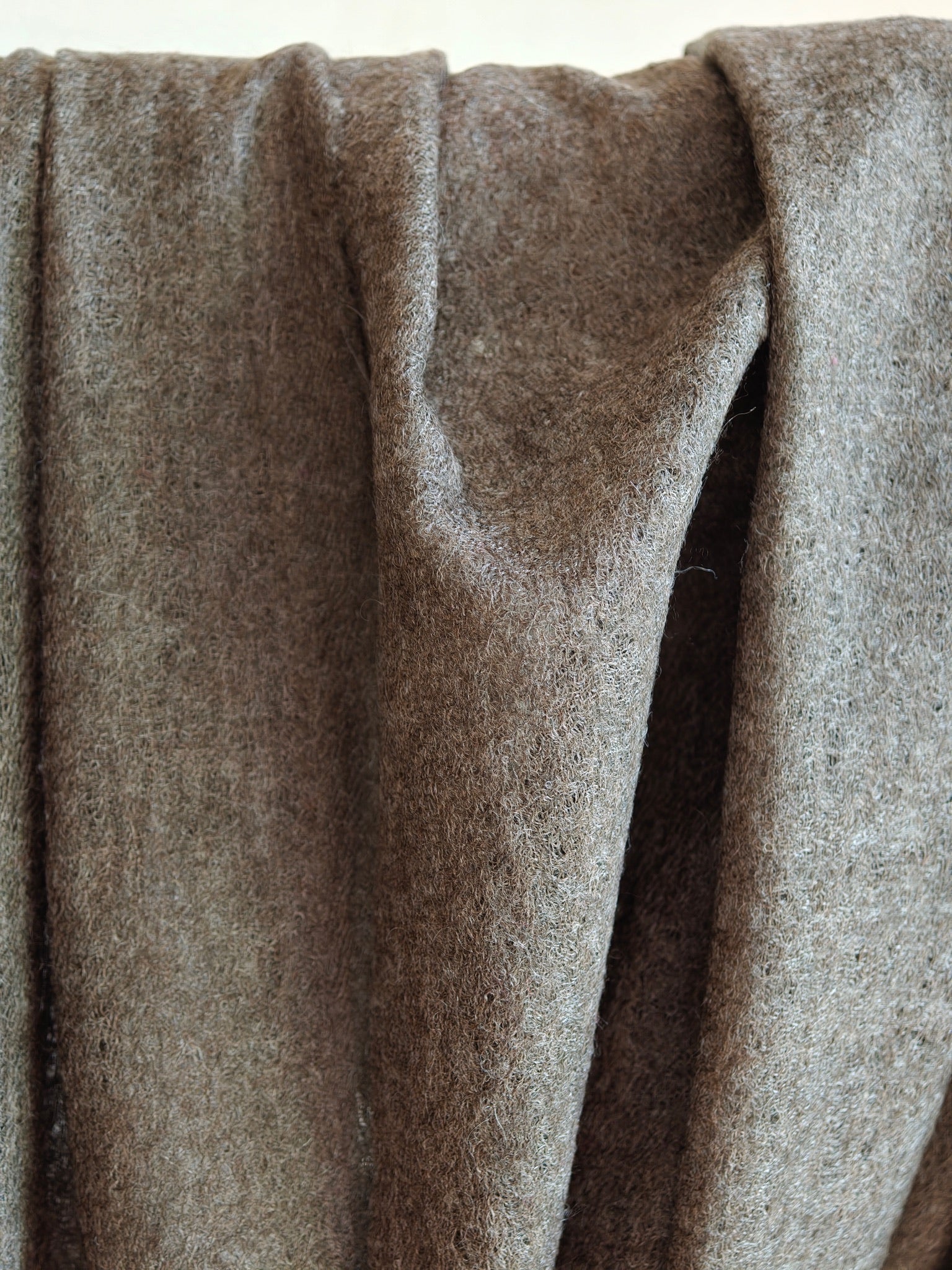 Detailed view of a lightweight brown cashmere shawl showing its semi sheer weave, airy texture, and natural wool fibers. Light filtering through the fabric emphasizes its breathability, softness, and handcrafted quality.