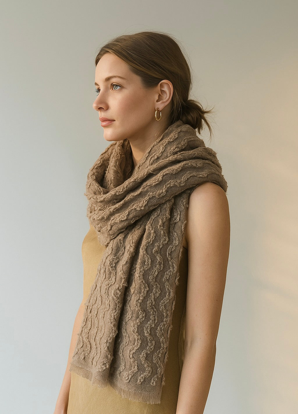 Woman wearing a large brown knitted scarf against a plain background