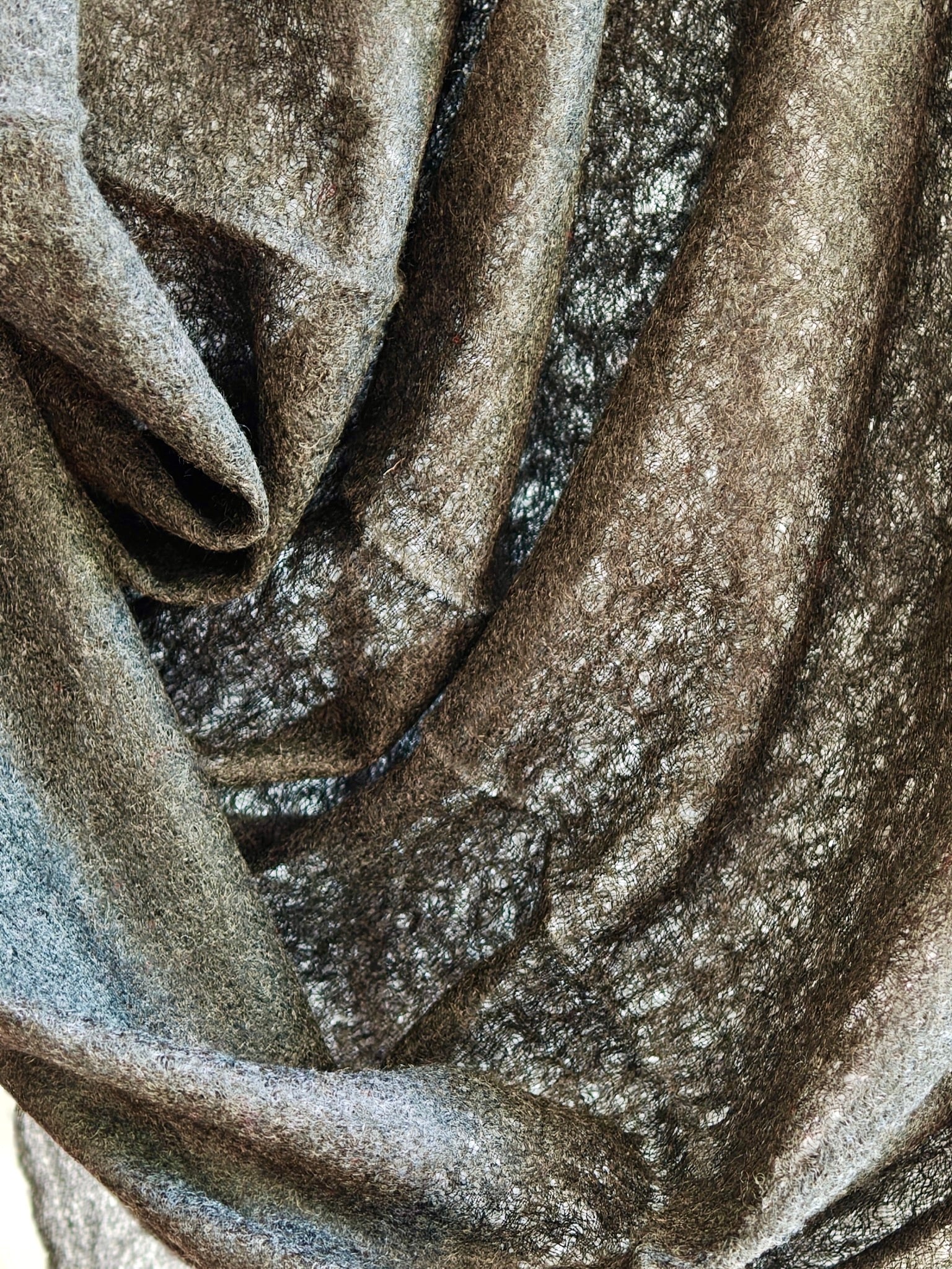 Draped cashmere fabric showing rich charcoal brown tones and airy gauze texture for a soft and elegant wrap.