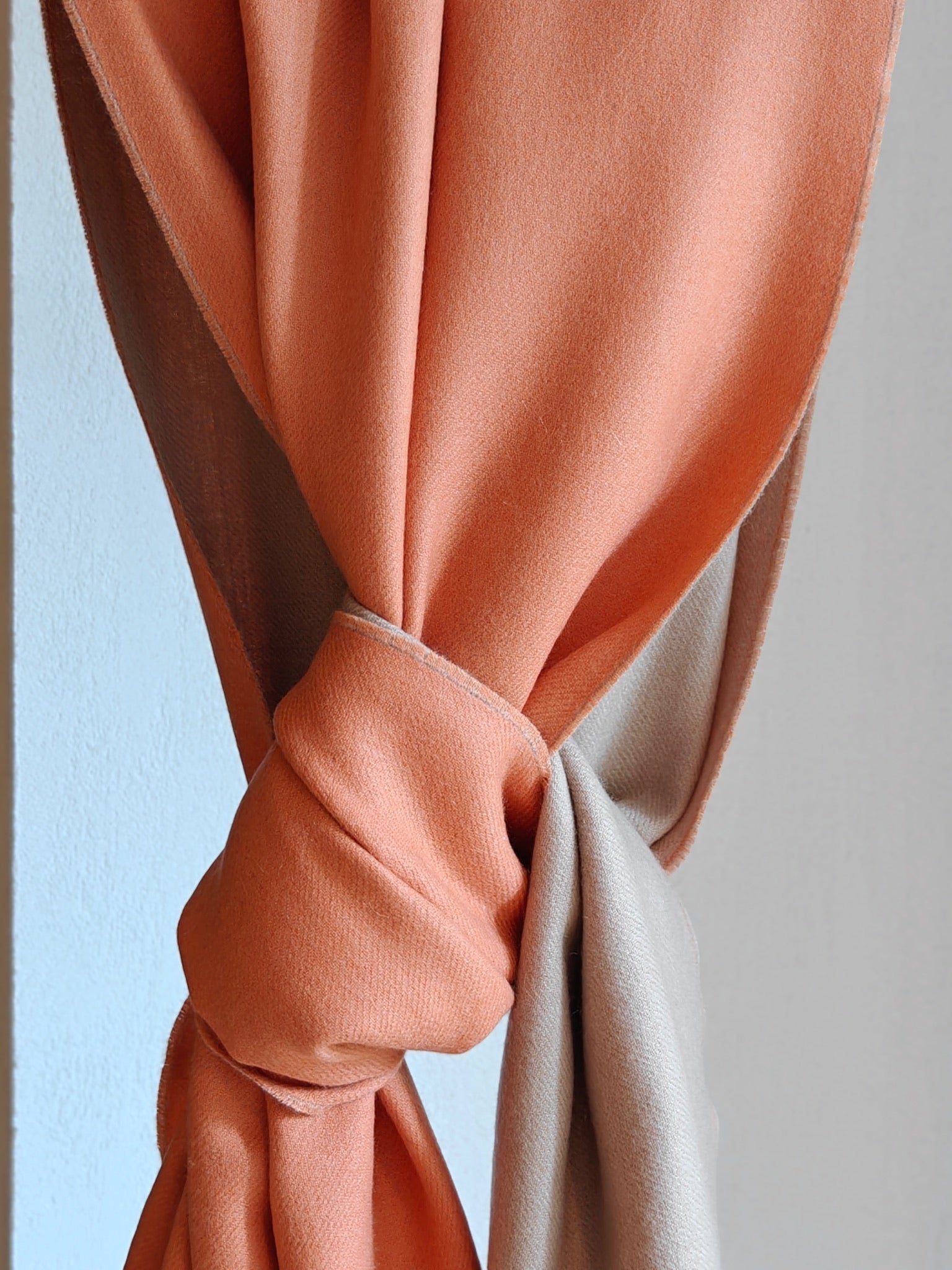 A close knot detail of the reversible cashmere wrap, capturing the fabric’s smooth weave, plush hand feel, and elegant two tone design. The gentle twist shows the wrap’s flexibility and refined drape.