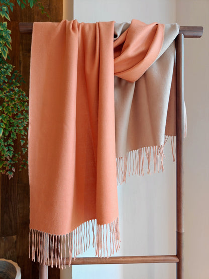 A full draped view of the coral and beige reversible cashmere wrap displayed on a wooden rack. The image highlights the wrap’s silky texture, fluid movement, and soft fringe detailing.