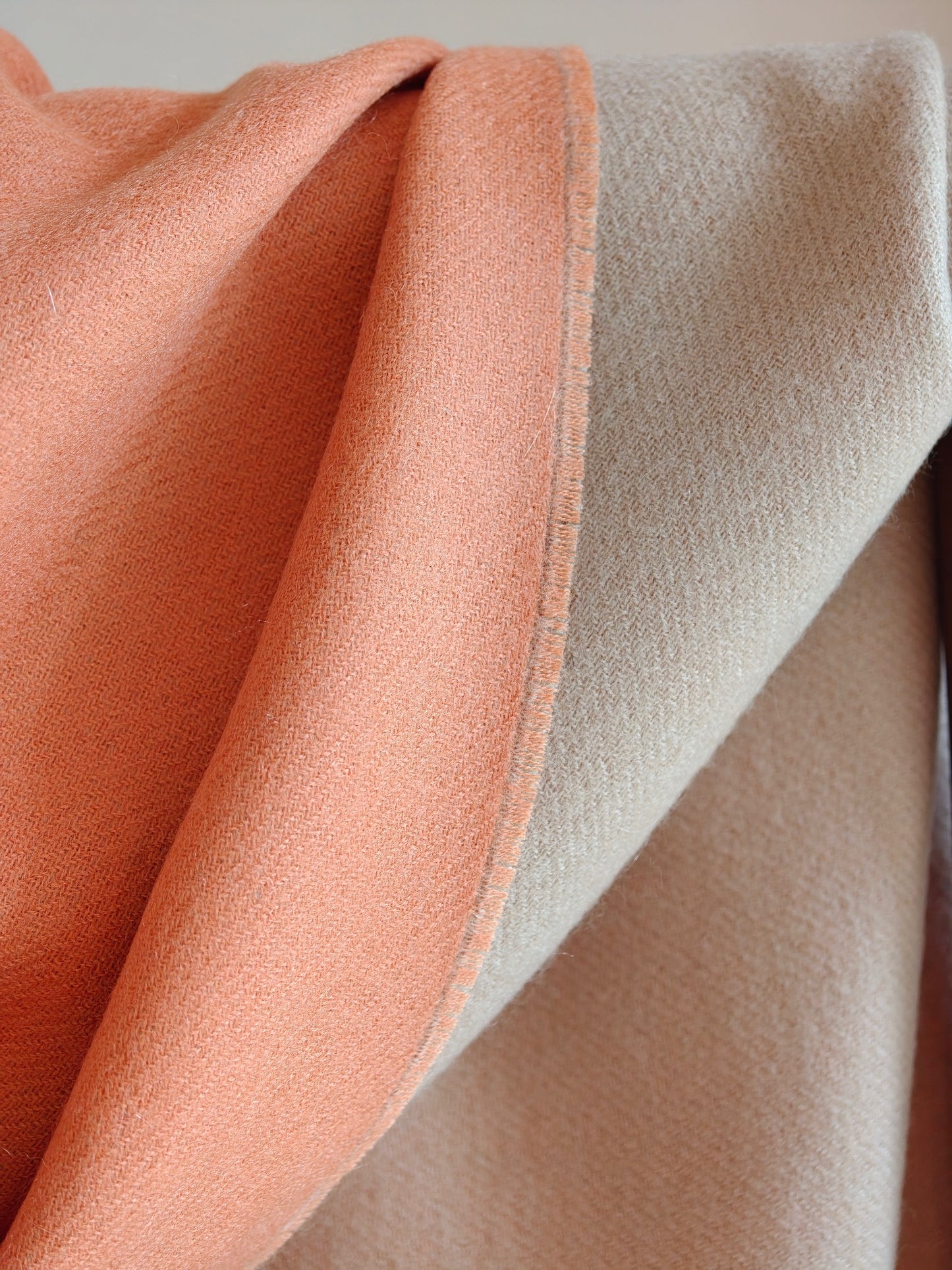 A detailed view of the reversible coral and beige cashmere wrap, showcasing the clean edge stitching and smooth double sided weave. The photo highlights the craftsmanship, softness, and elegant color contrast.