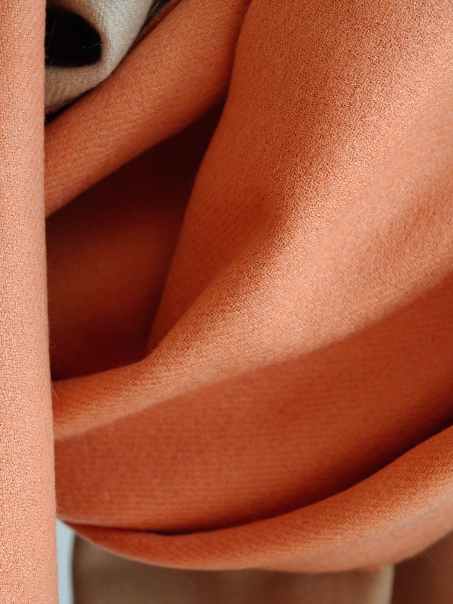 A close up of the coral cashmere wrap showing its smooth, ultra fine weave and soft natural drape. The detailed texture highlights the fiber’s lightweight warmth and luxurious finish.