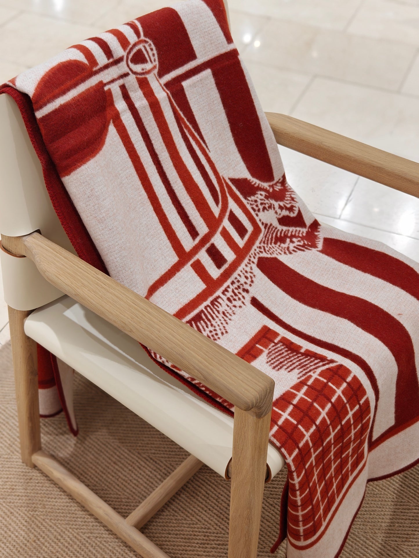 A full view of the red equestrian wool throw arranged across a chair, showing its complete pattern, vivid color blocking, and cozy woven texture.