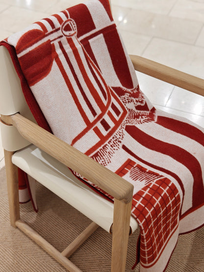 A full view of the red equestrian wool throw arranged across a chair, showing its complete pattern, vivid color blocking, and cozy woven texture.