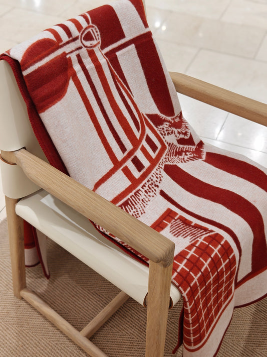 A full view of the red equestrian wool throw arranged across a chair, showing its complete pattern, vivid color blocking, and cozy woven texture.