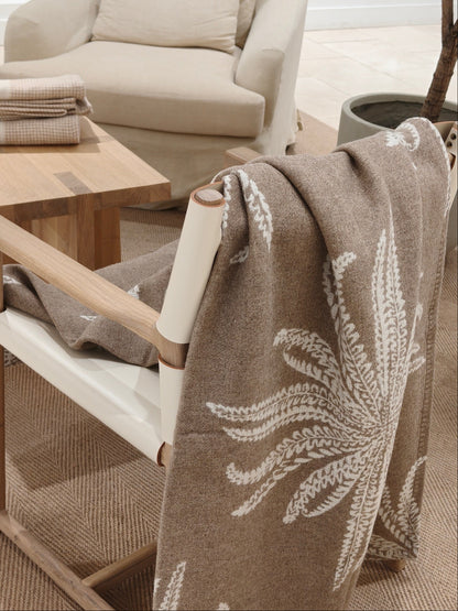 The wool throw draped over the back of a chair, revealing its elegant botanical pattern and plush texture. The natural color palette creates a calm, inviting look.