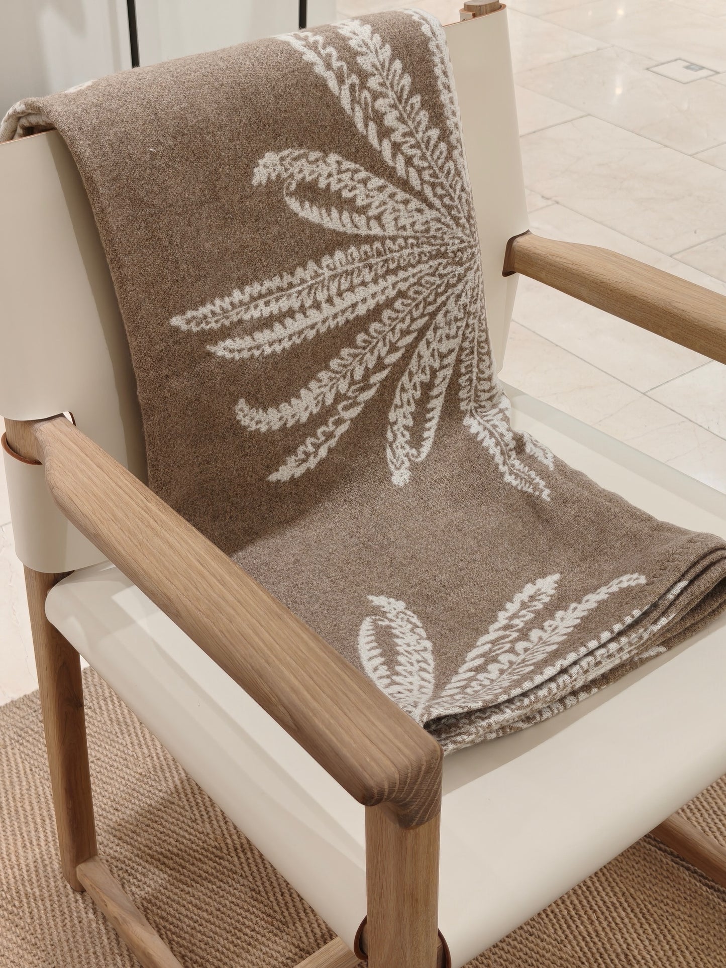 A folded view of the fawn wool throw arranged neatly on a chair. The smooth surface and crisp botanical pattern highlight the throw’s quality and craftsmanship.