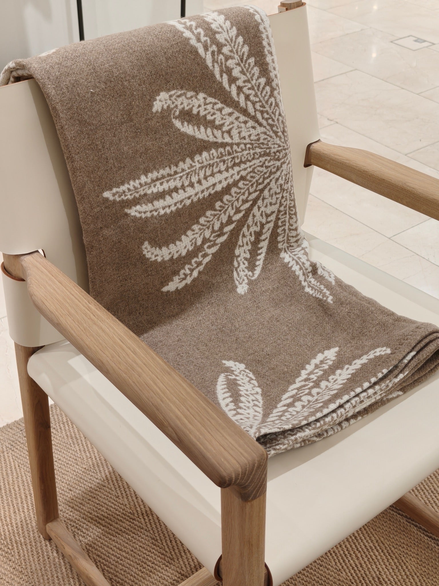 A folded view of the fawn wool throw arranged neatly on a chair. The smooth surface and crisp botanical pattern highlight the throw’s quality and craftsmanship.