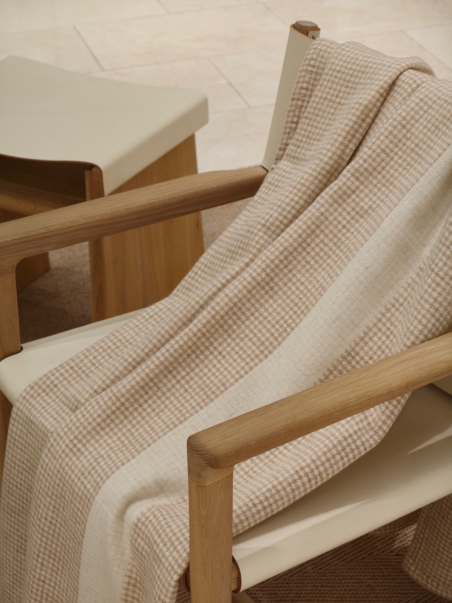 A softly draped wool throw displayed over a chair, highlighting its gentle movement, smooth weave, and understated houndstooth design.