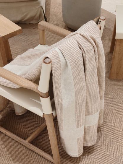 A layered side view of the wool throw resting over a chair, capturing its elegant folds, subtle check pattern, and warm natural texture.