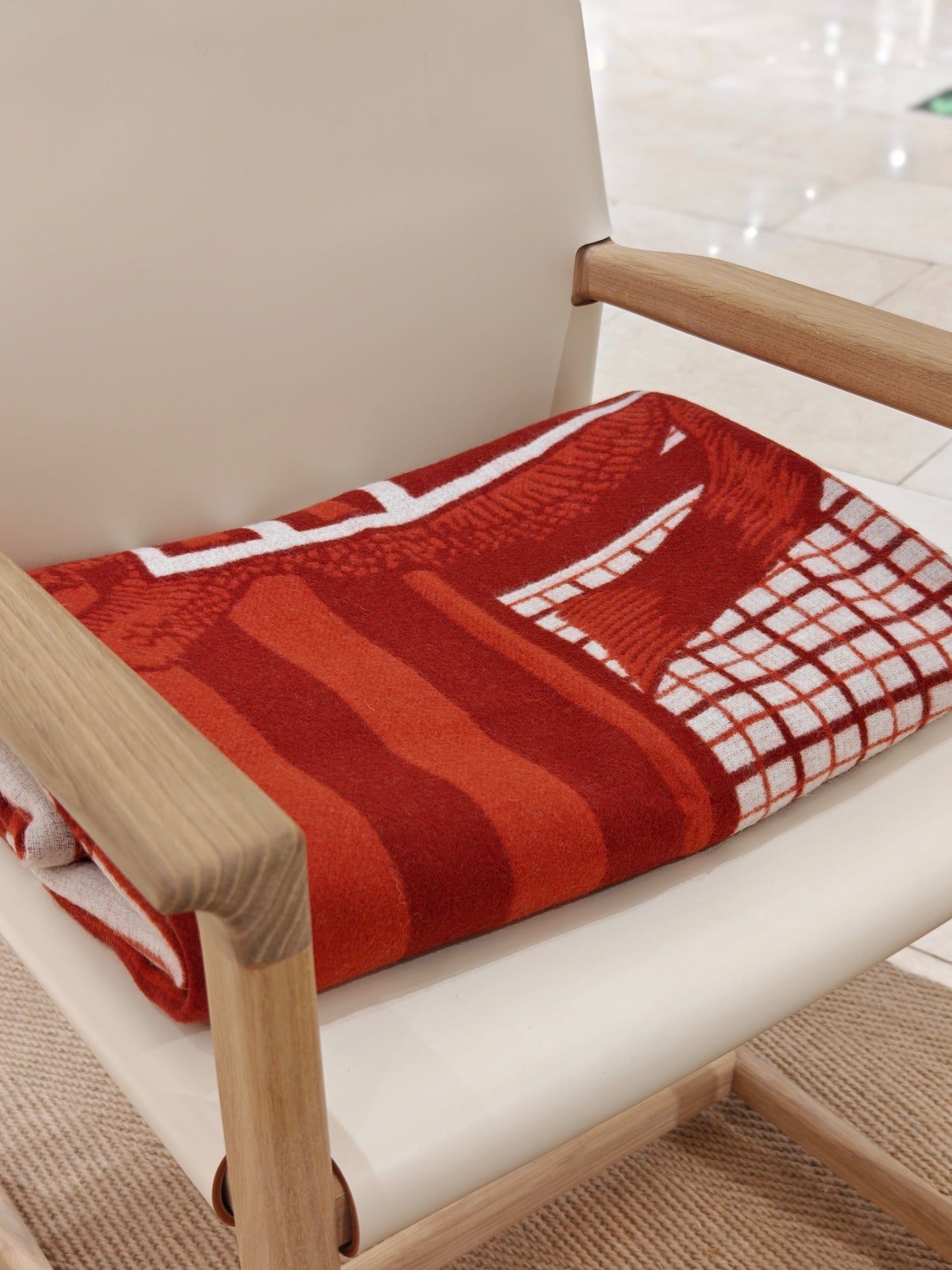 A folded red equestrian wool throw displayed on a minimalist chair, highlighting its rich red tones, crisp white pattern, and plush warmth.