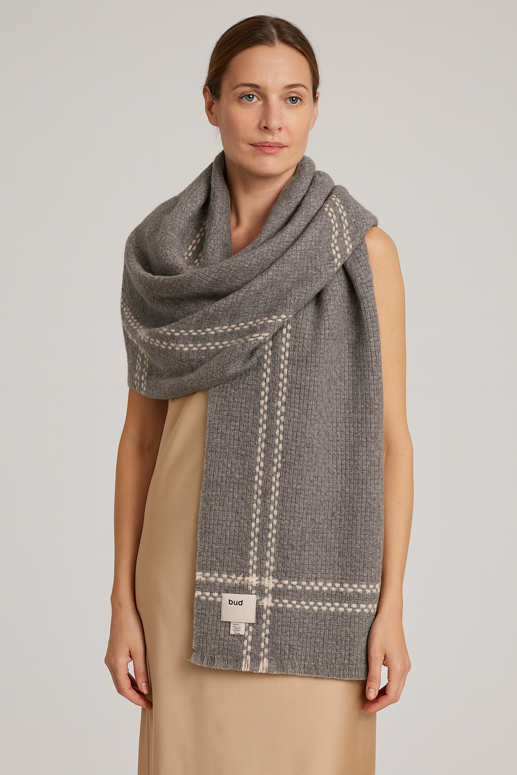 A soft gray cashmere wool scarf draped naturally on a female model in her mid 30s, showcasing the textured waffle knit pattern and white windowpane detailing. Classic quiet luxury styling with a neutral studio background, highlighting the scarf’s premium Inner Mongolian craftsmanship.
