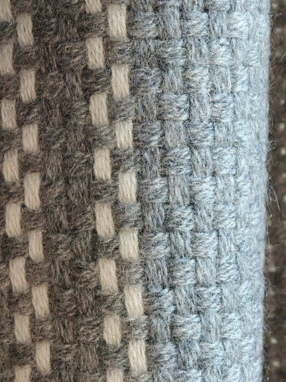 A detailed close up of the gray cashmere wrap showing its soft woven texture and ivory plaid accents. The image highlights the natural loft, warmth, and craftsmanship of the Inner Mongolian cashmere fiber.