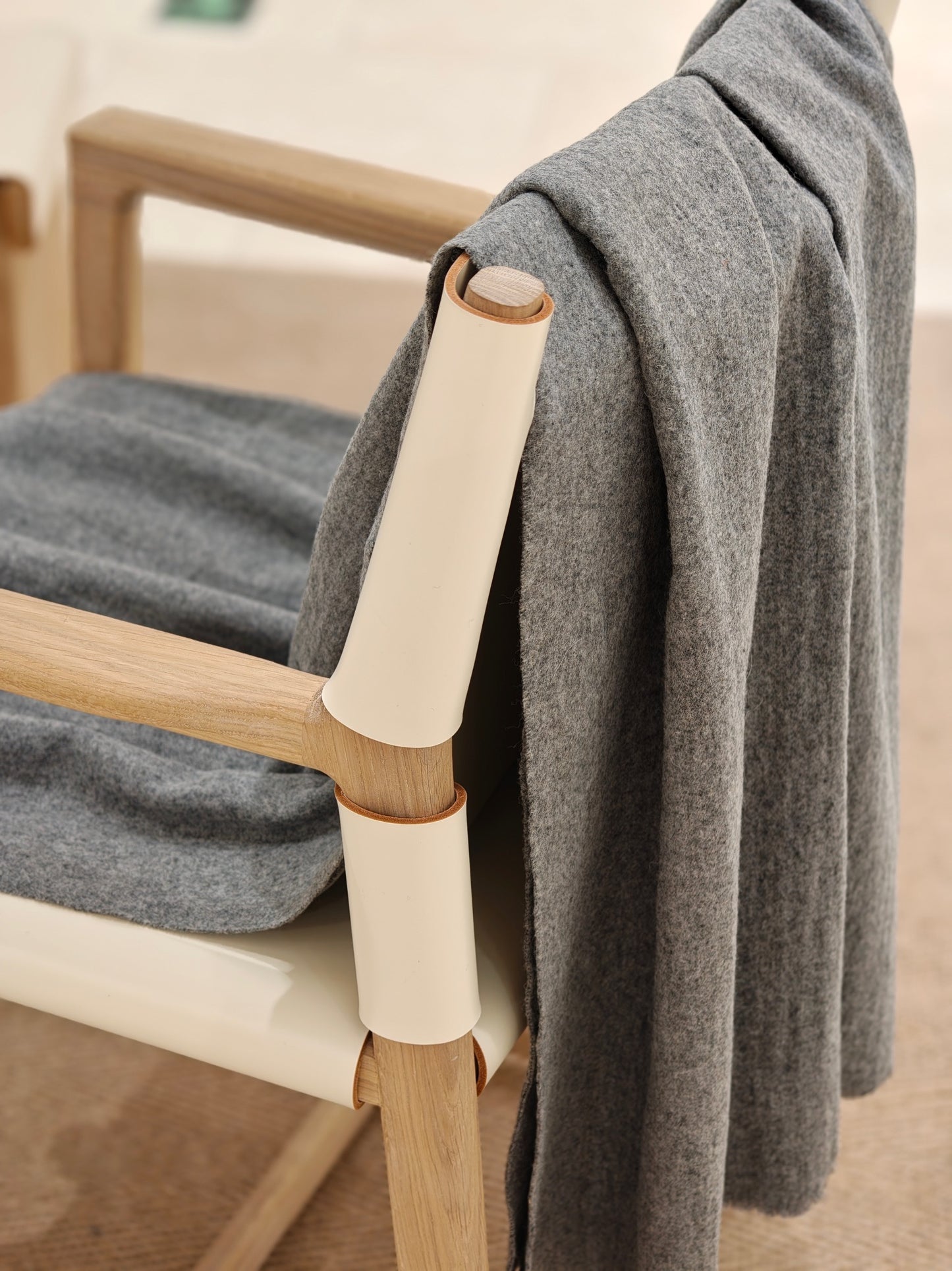 A gray wool throw draped over a wooden chair, showing its smooth surface and relaxed natural folds. The soft texture and cool neutral tone create an understated, elevated home look.