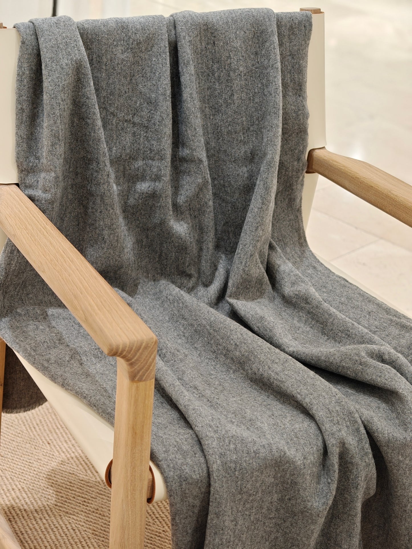 The gray wool throw draped over the chair in a relaxed full view, highlighting its fluid movement and cozy, brushed texture. A simple, modern styling that fits seamlessly into any space.