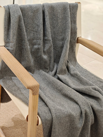 The gray wool throw draped over the chair in a relaxed full view, highlighting its fluid movement and cozy, brushed texture. A simple, modern styling that fits seamlessly into any space.