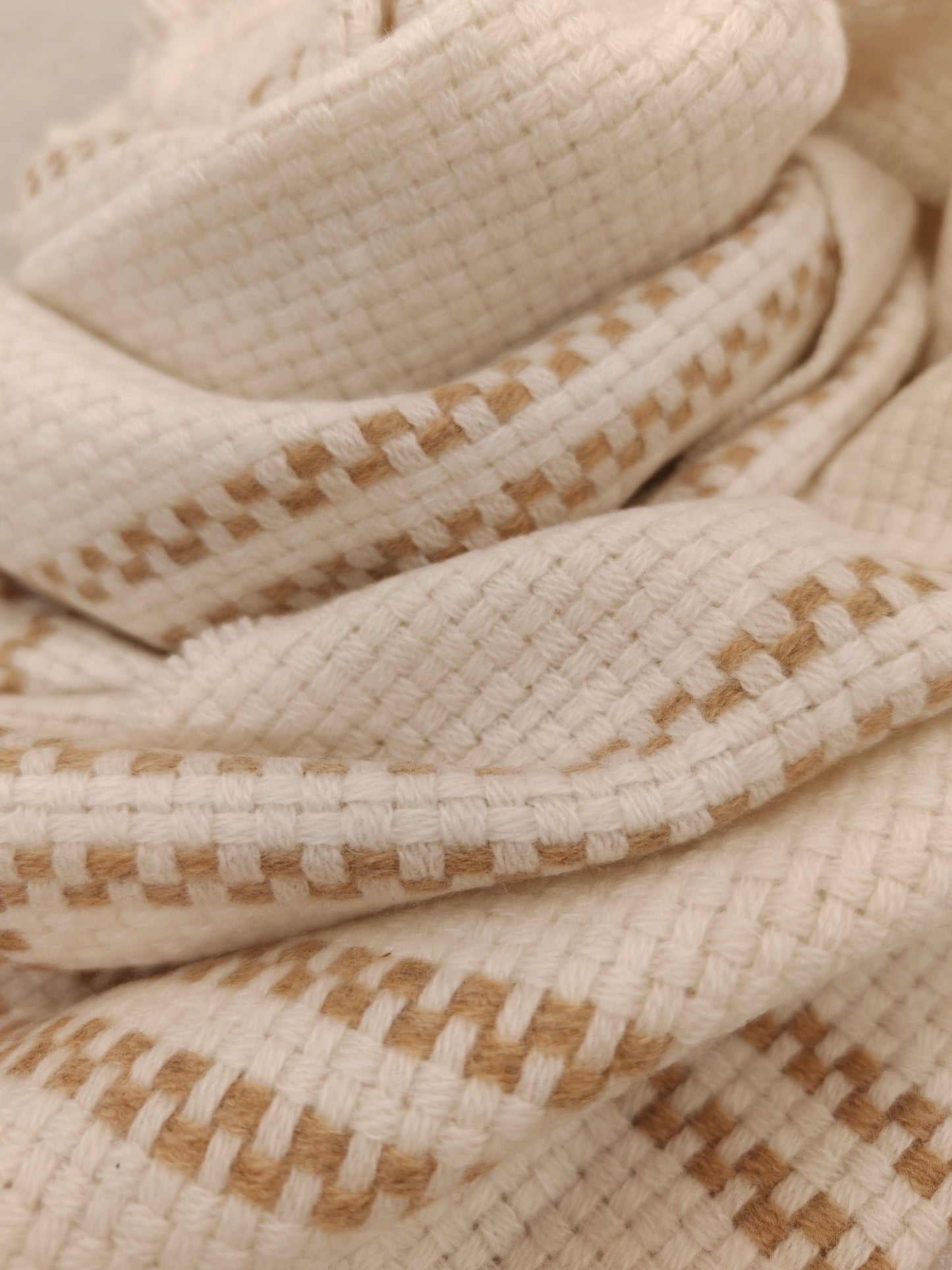 A soft folded view of the ivory cashmere wrap featuring a warm beige plaid pattern and a textured waffle weave. The close up captures the wrap’s plush feel, drape, and artisanal finish.