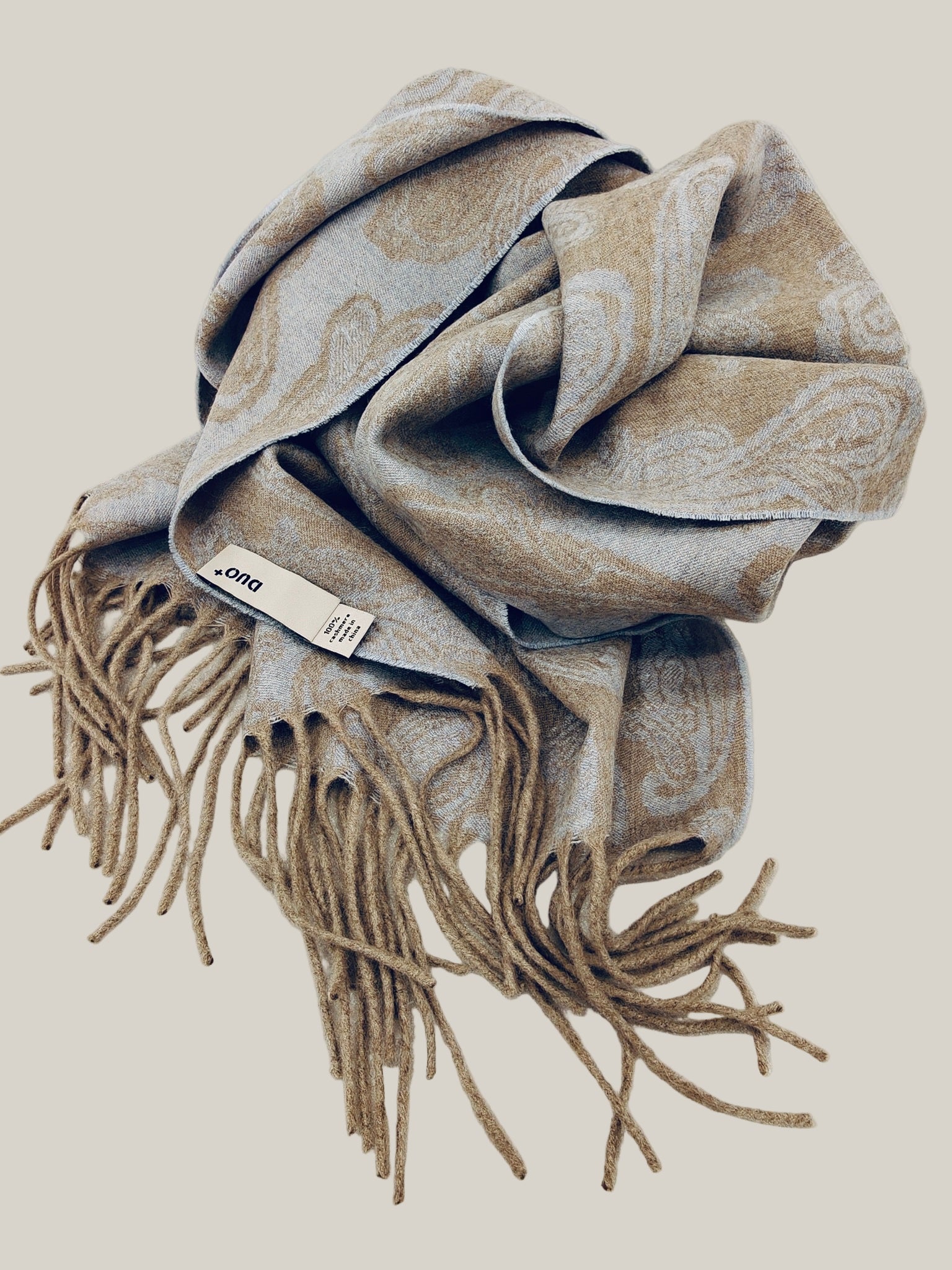 Soft folded view of a pure cashmere paisley scarf featuring a reversible beige and blue design and long fringe. Highlights the plush texture and premium quality of Duo Plus cashmere.