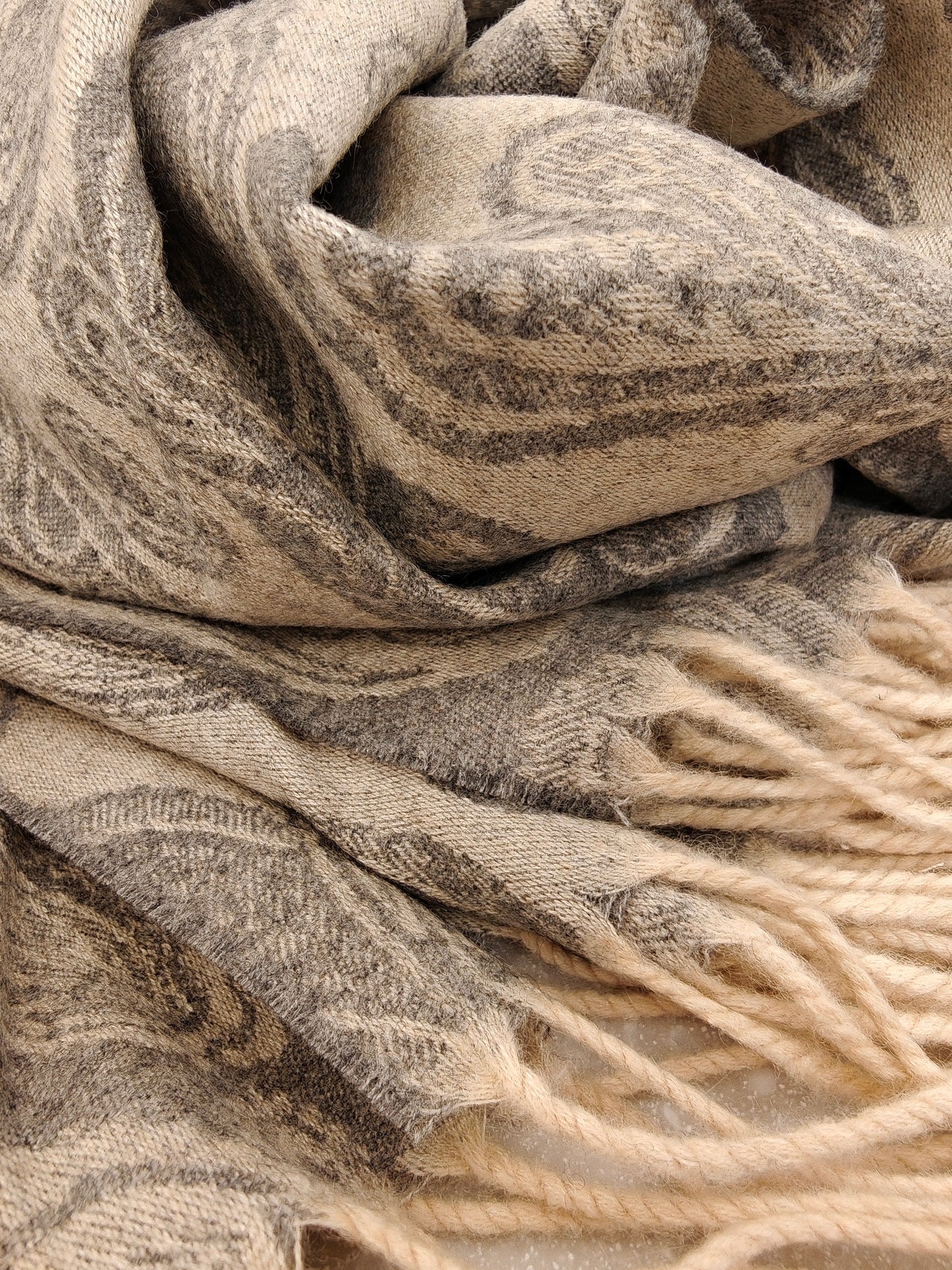 Close up of a pure cashmere paisley scarf from Duo Plus in natural brown and taupe tones. Shows the soft brushed cashmere texture and thick twisted fringe detail.