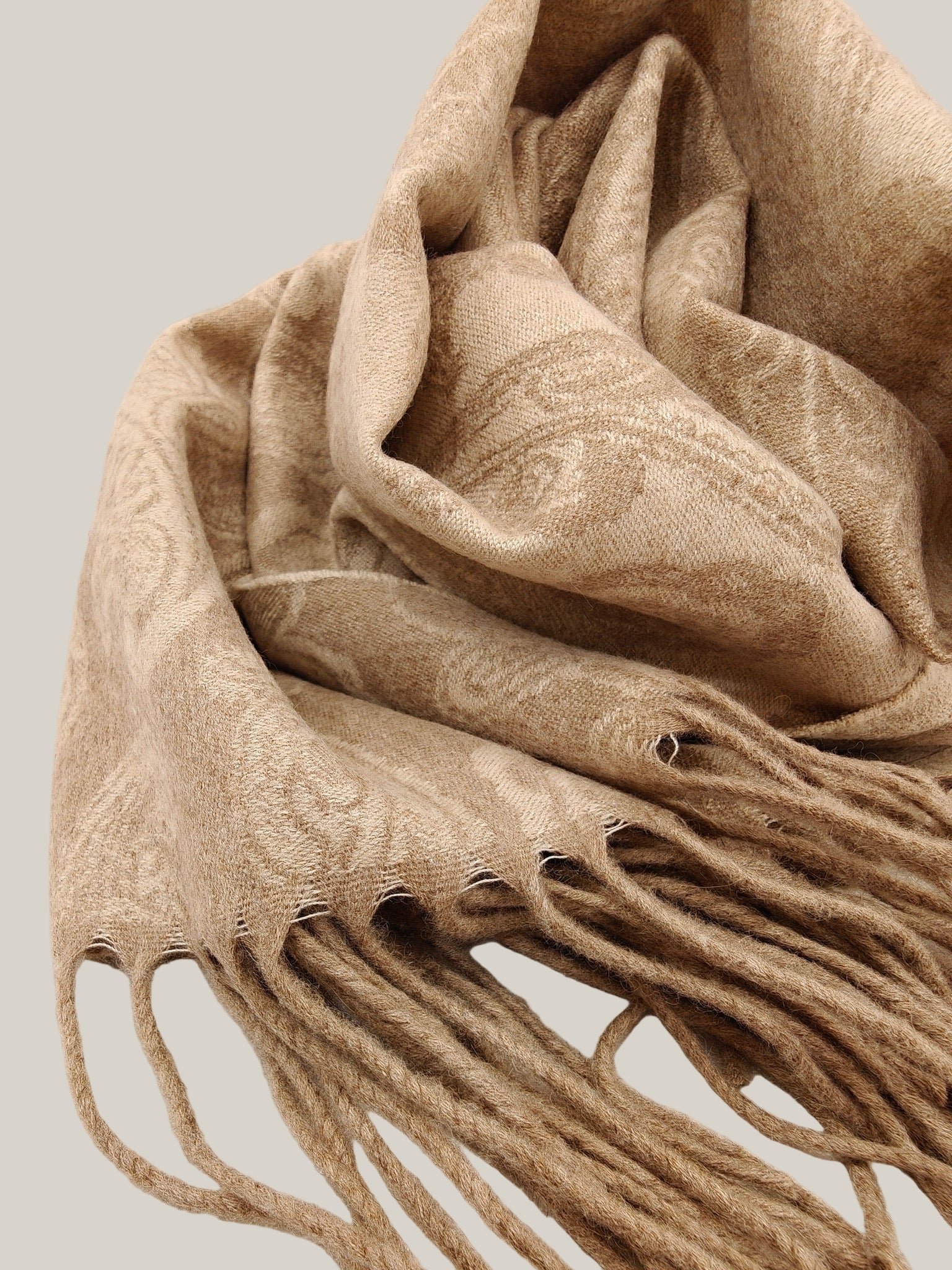 Close up of a pure cashmere paisley scarf from Duo Plus in soft taupe beige. Shows the detailed woven paisley pattern and plush twisted fringe. Highlights the lightweight texture of Inner Mongolian cashmere.