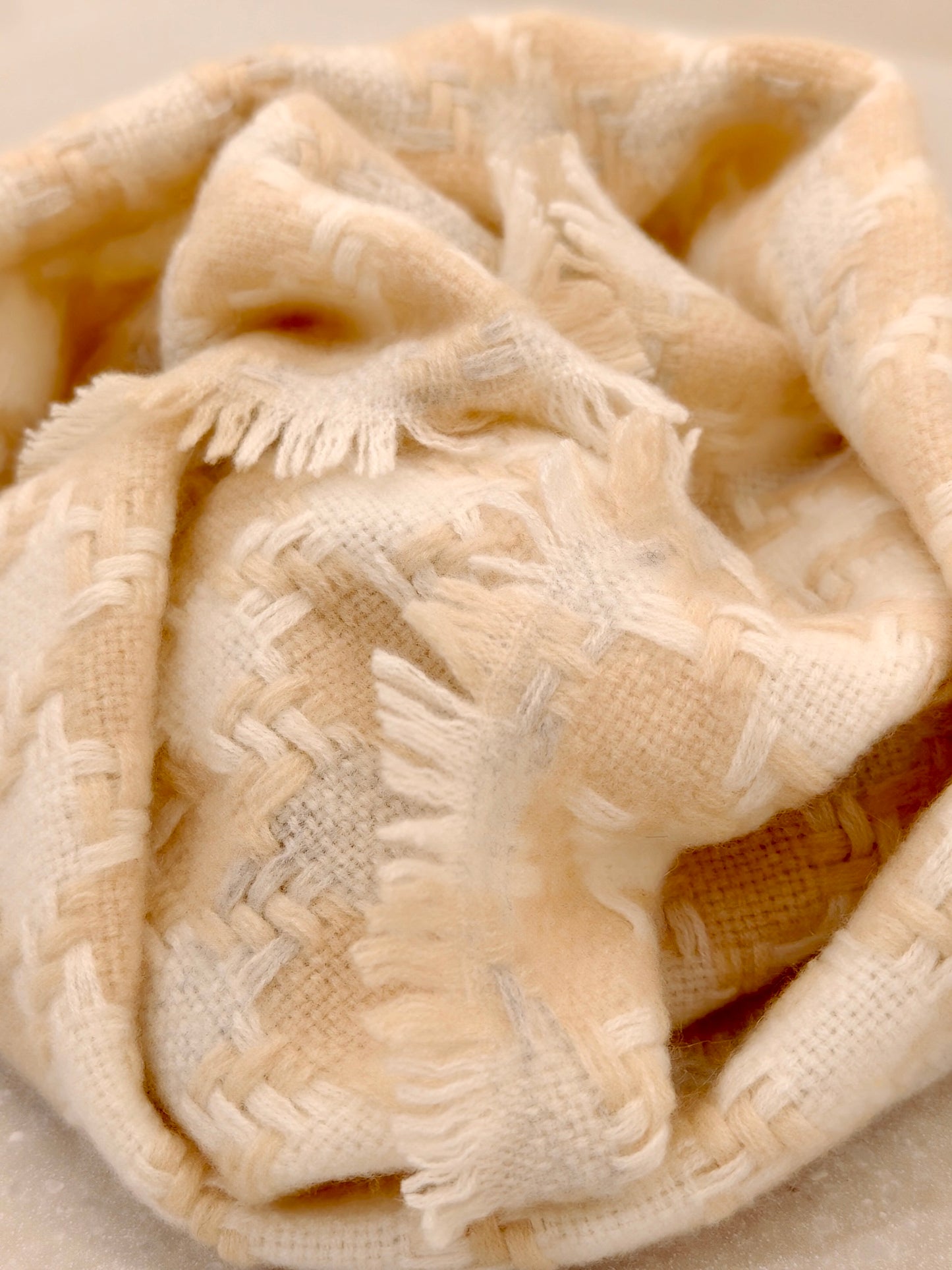 Close up of a pure cashmere textured scarf from Duo Plus in soft cream and beige. Shows the plush woven pattern, airy hand feel, and delicate fringe detail. Highlights the premium Inner Mongolian cashmere texture.