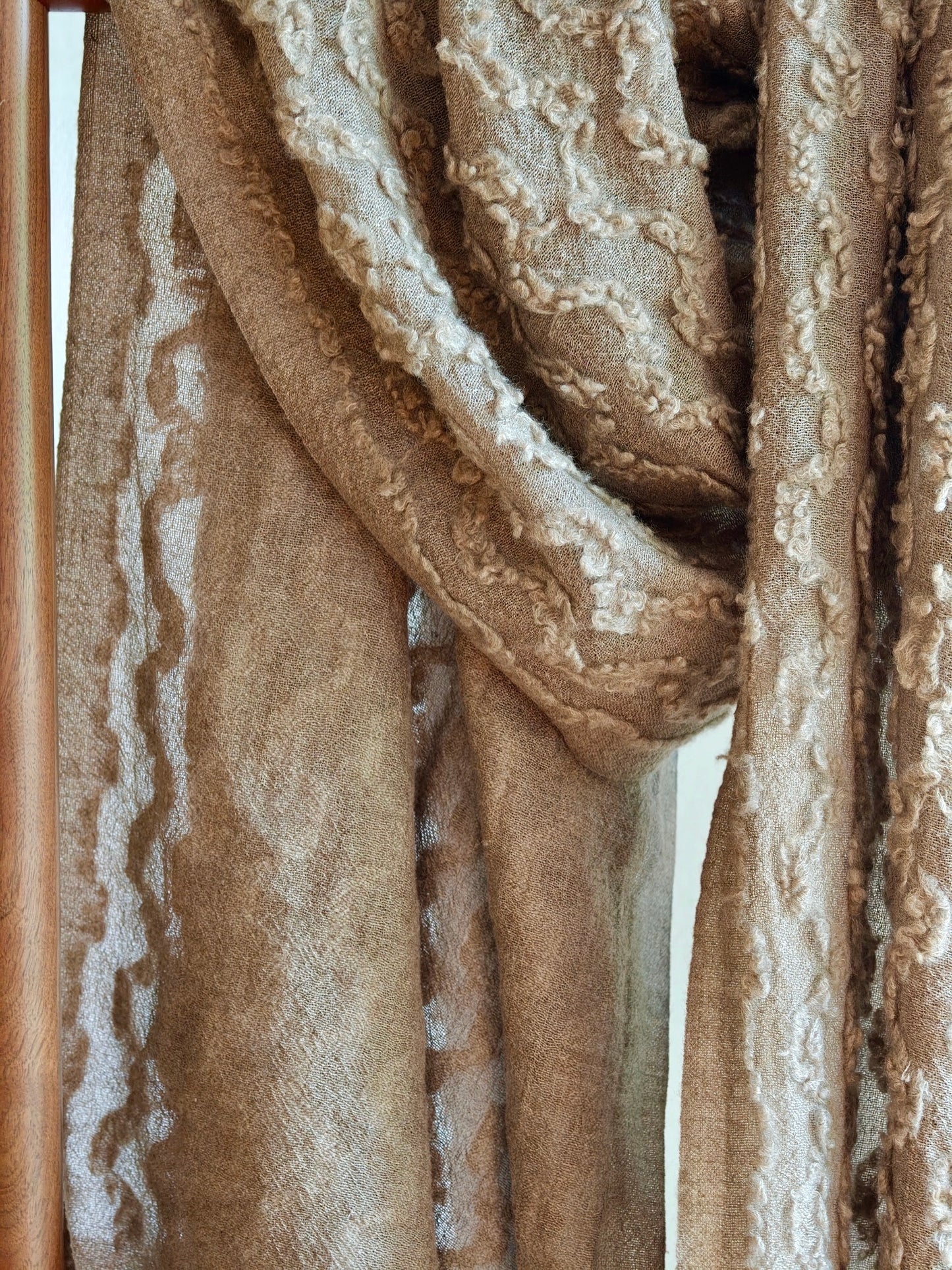 The Ripples Cashmere Wrap draped over a rack, revealing the signature raised ripple pattern and soft sheen. The natural folds emphasize its depth and artisanal craftsmanship.