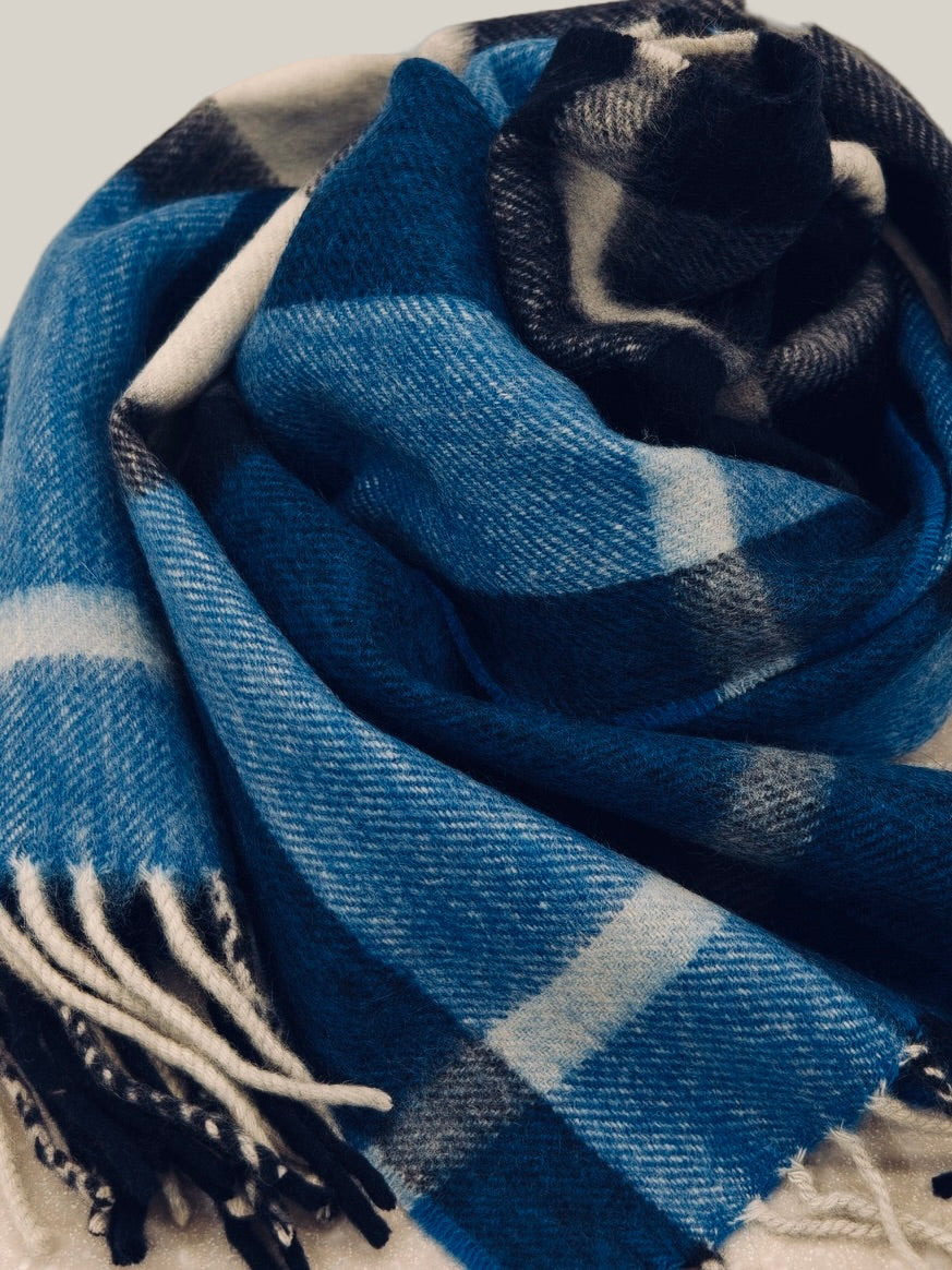 Slim blue cashmere scarf with a classic plaid pattern in navy, white, and charcoal. The brushed cashmere texture gives a soft hand feel and lightweight warmth ideal for winter layering.