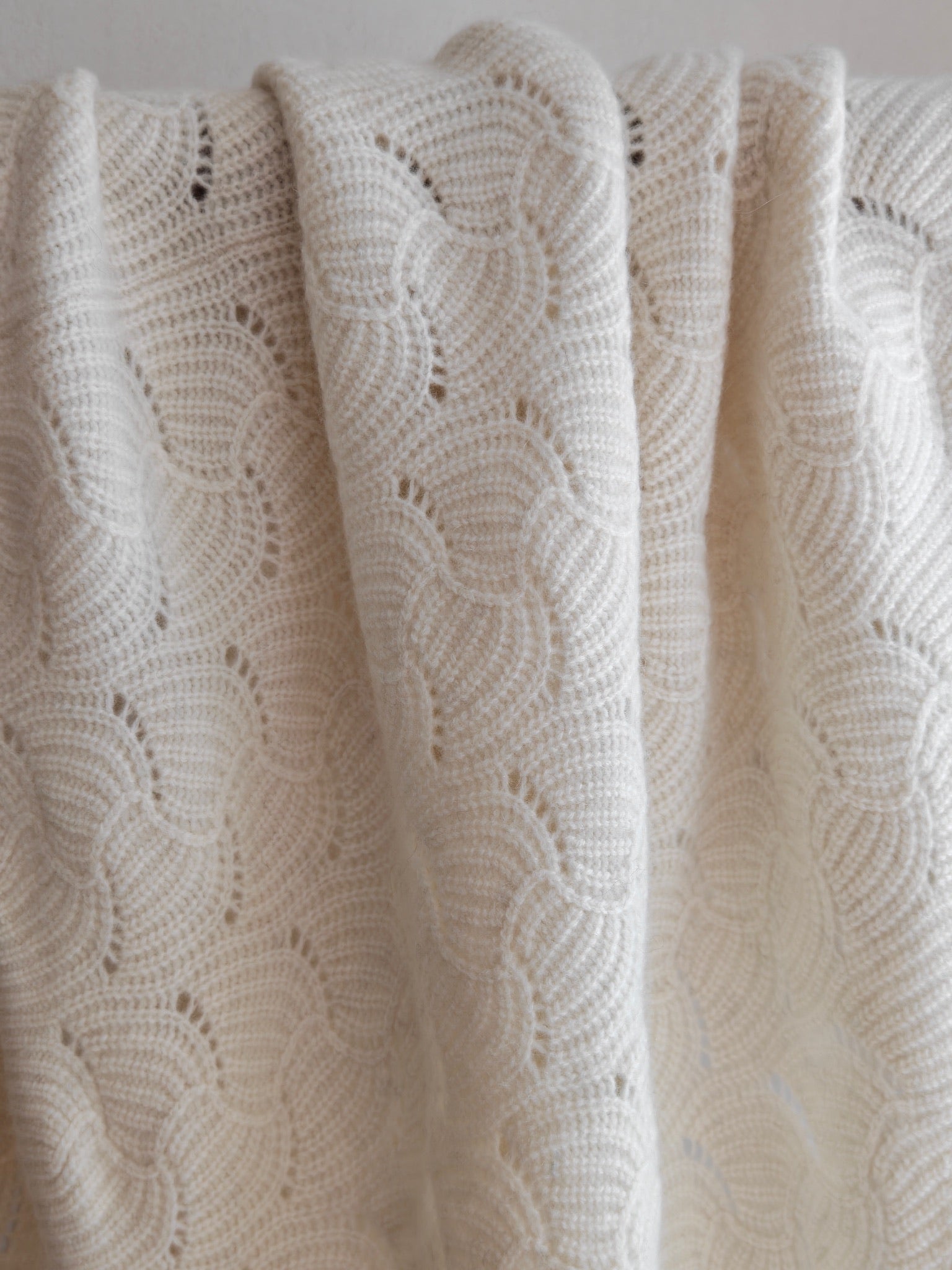 Soft draped view of the ivory yak wool blend shawl hanging over a rod, focusing on its scalloped knit and natural texture.